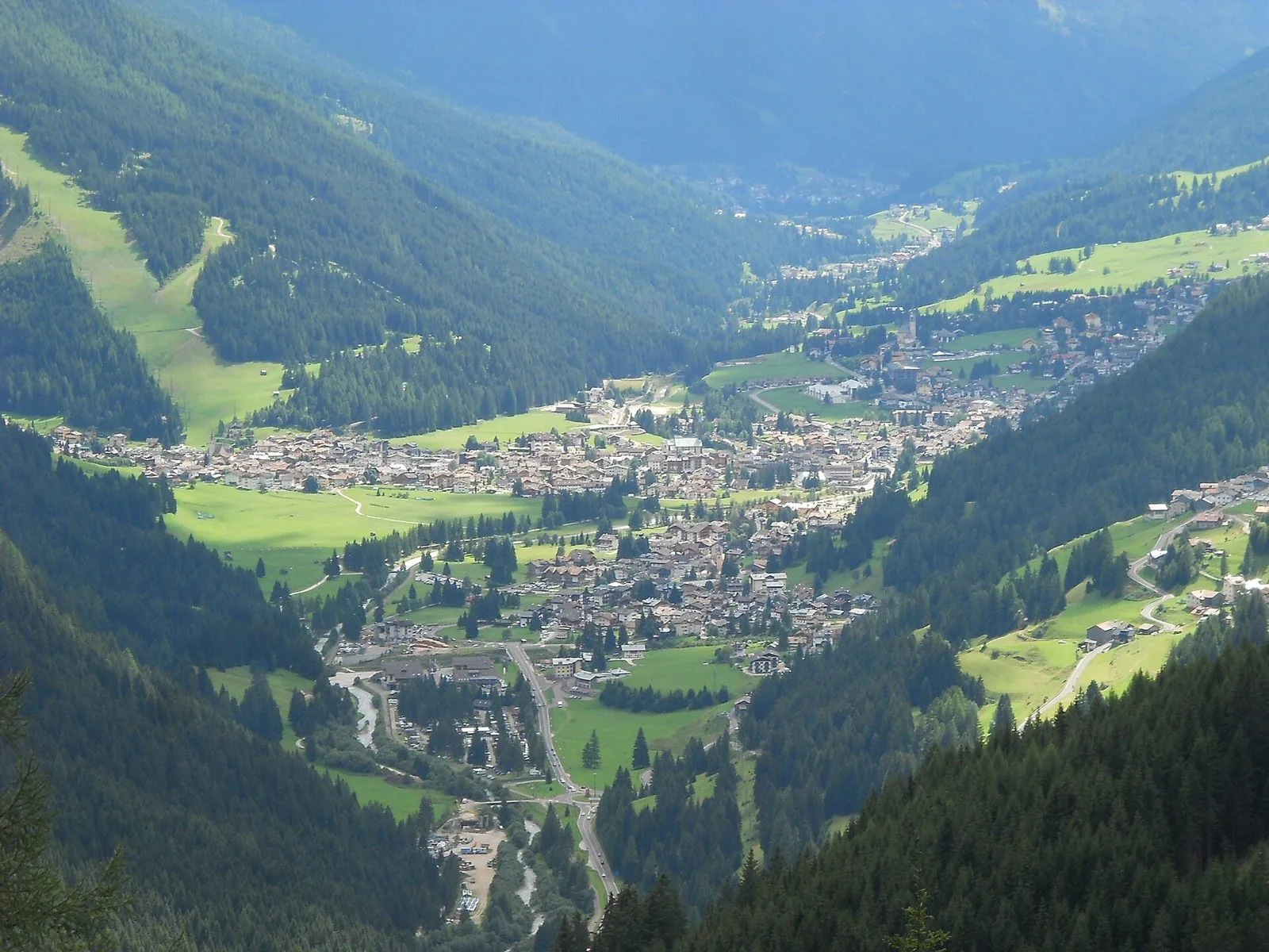 Veduta dall'alto del fondovalle della Val di Fassa con gli abitati di Pozza e Vigo tra prati verdi e boschi di conifere