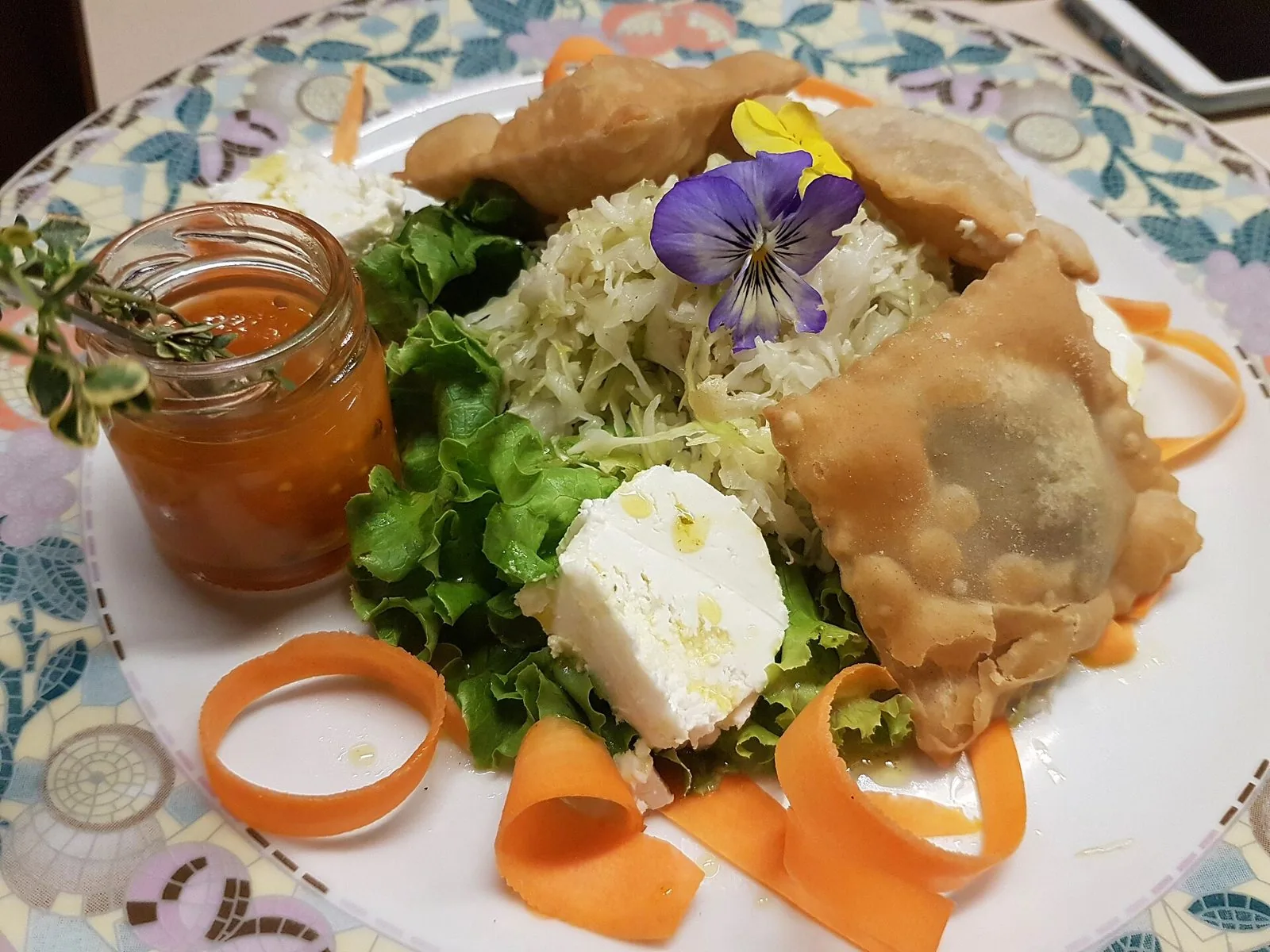 Piatto con tre turtres fritte e dorate, insalata di cavolo cappuccio, lattuga, formaggio fresco, nastri di carota, una viola commestibile e un vasetto di salsa
